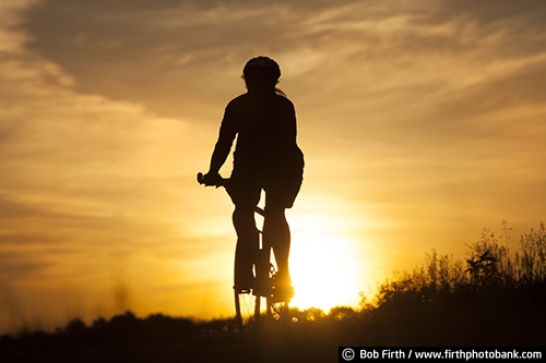 sunset;bicycle touring;bicycling;bikes;cycling;cyclist;fun pastime;exercise;recreation;Minnesota;MN;silhouette;summer;sun;woman;solitude;peaceful;relaxing;golden sky;mountain bike